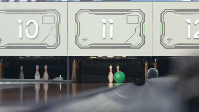 Asian person in casual outfit rolls a bowling ball smoothly on the lane toward the pins, captured indoors with clear background, showing focus, motion, and game preparation