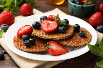 Tasty Dutch waffles (stroopwafels) with honey, berries and mint on wooden table, closeup