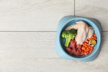 Feeding bowl with natural raw products for pet on white wooden floor, top view. Space for text