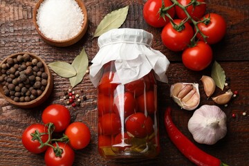Tasty pickled tomatoes in jar and ingredients on wooden table, flat lay