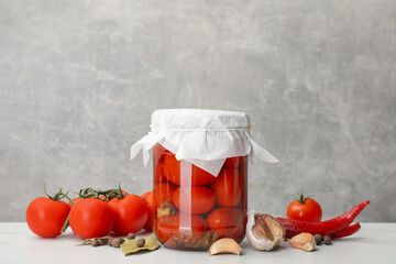 Tasty pickled tomatoes in jar, fresh products and spices on white table against grey background