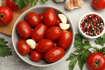 Tasty pickled tomatoes in bowl and ingredients on grey table, flat lay