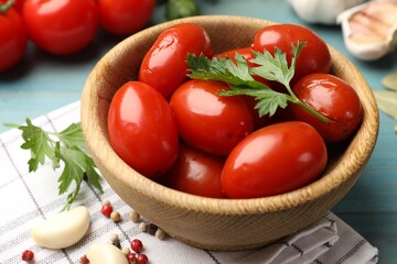 Tasty pickled tomatoes in bowl and ingredients on light blue table, closeup
