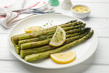 Tasty cooked asparagus served with lemon and thyme on white wooden table, closeup