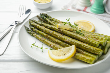 Tasty cooked asparagus served with lemon and thyme on white wooden table, closeup