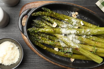 Tasty cooked asparagus served with parmesan on black wooden table, flat lay