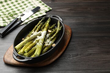 Tasty cooked asparagus served with parmesan on black wooden table, space for text