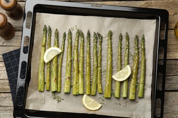 Tasty cooked asparagus and lemon on baking tray on wooden table, top view