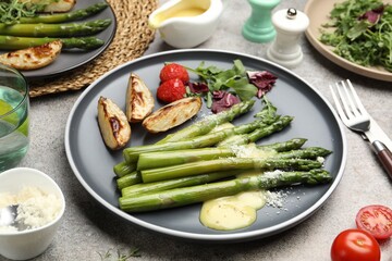 Tasty cooked asparagus served with baked potatoes, tomatoes and sauce on grey table, closeup