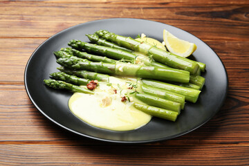 Tasty cooked asparagus served with lemon and sauce on wooden table, closeup