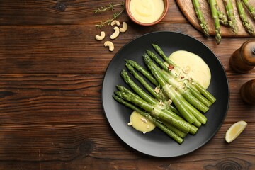 Tasty cooked asparagus served with sauce on wooden table, flat lay. Space for text