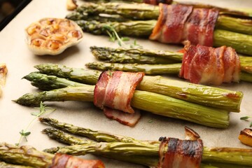 Tasty cooked asparagus with bacon and spices on parchment paper, closeup