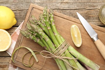 Fresh raw asparagus spears, knife and lemon on wooden table, flat lay