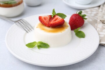 Tasty panna cotta with caramel, strawberries and mint on light table, closeup