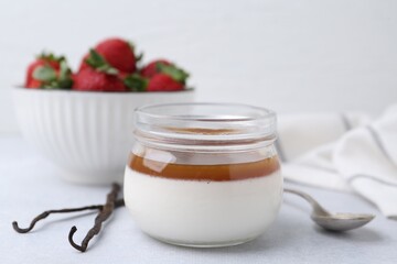 Tasty panna cotta with caramel, vanilla pods and strawberries on light table, closeup