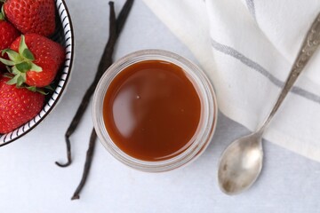 Tasty panna cotta with caramel, vanilla pods and strawberries on light table, flat lay