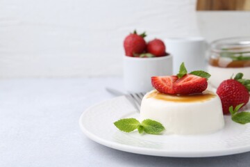 Tasty panna cotta with caramel, strawberries and mint on light table, closeup. Space for text