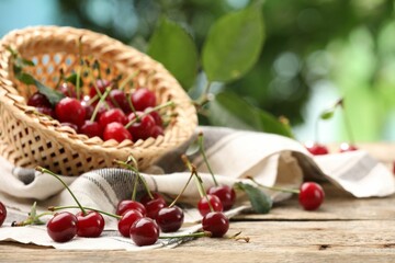 Fresh cherries and wicker basket on wooden table against blurred green background, closeup