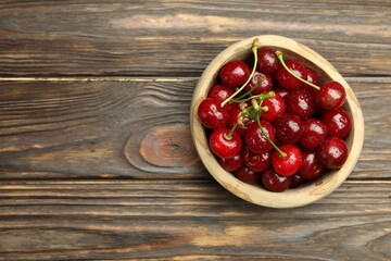 Fresh wet cherries in bowl on wooden table, top view. Space for text