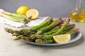 Fresh raw asparagus and lemon on light grey table, closeup