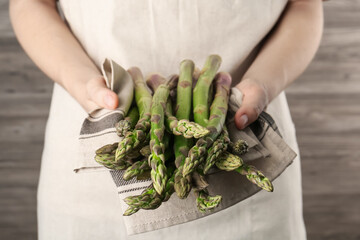 Woman holding fresh raw asparagus near wooden wall, closeup