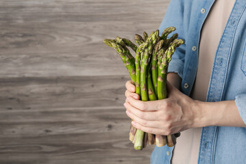 Woman holding fresh raw asparagus near wooden wall, closeup. Space for text