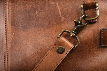 A close-up view focuses on the rich, textured brown leather of a bag, highlighting a strap with a...
