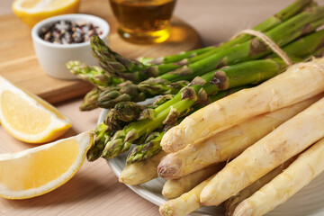 Different raw asparagus spears and spices on wooden table, closeup