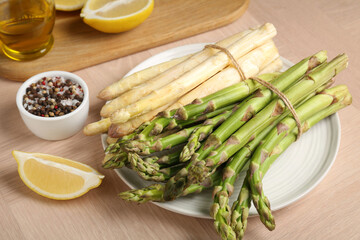 Different raw asparagus spears and spices on wooden table, above view