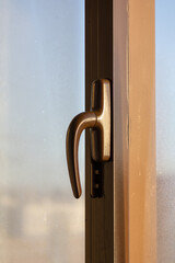 Window with a handle that is slightly open. The handle is made of metal and is slightly rusted. The window is located in a room with a view of the outside