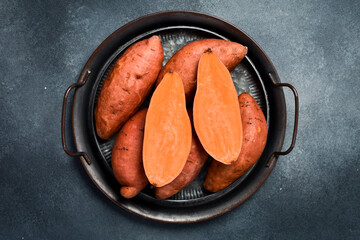Close up of raw organic sweet potatoes. On a tray. Gray stone background.