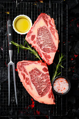 Two raw marble ribeye steaks are prepared over hot coals. On a black charcoal background. Top view.