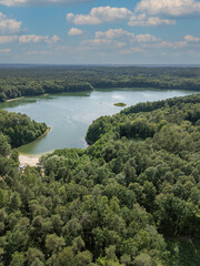 Aerial panoramic view of a clear-water lake at sunrise, surrounded by forest. Treetops are...