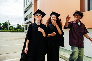 Three joyful young graduates share laughter and excitement after their graduation ceremony. Dressed...