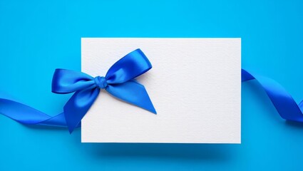 Blank gift greeting card ribbon below and blue bright and shiny ribbon bow on left side isolated on luxury blue background.