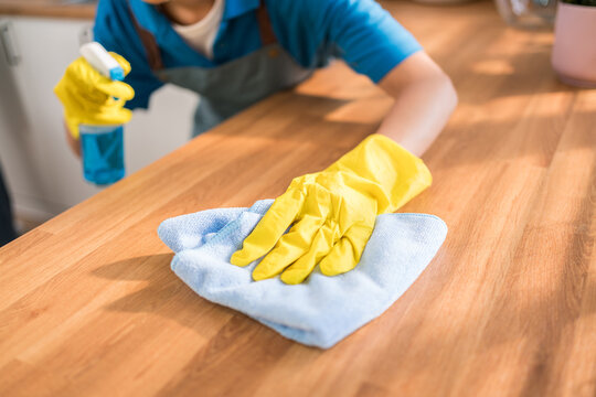 Close-up of a professional cleaner wiping a wooden kitchen counter with a blue microfiber cloth and spray bottle, emphasizing hygiene, sanitation, and premium home cleaning service standards.