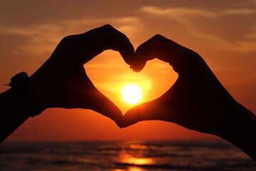 hand making a heart shape on the beach at sunset. a person making a heart shape with their hands. a person taking a picture of a sunset