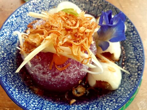 Overhead shot of Thai traditional Som Chun dessert with fermented lychee, butterfly pea ice and fried shallot in blue patterned bowl, fushion Thai Royal Desert