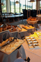Buffet table with assorted cakes, pastries, croissants, and small dessert bowls. Elegant restaurant interior with natural light and cozy atmosphere