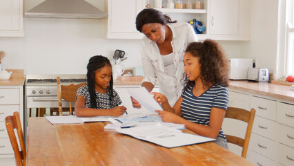 Mother Helping Two Daughters Sitting At Table Doing Homework