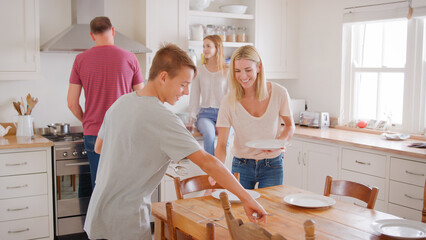 Family With Teenage Children Laying Table For Meal In Kitchen
