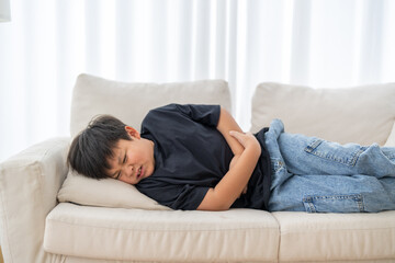 Portrait of sick unhappy little child asian boy touching belly stomach with suffering from stomach...