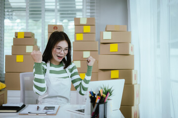 A young Asian woman entrepreneur in a striped shirt and apron works from her home office, managing e-commerce inventory, packaging orders, and organizing shipping for online customers.