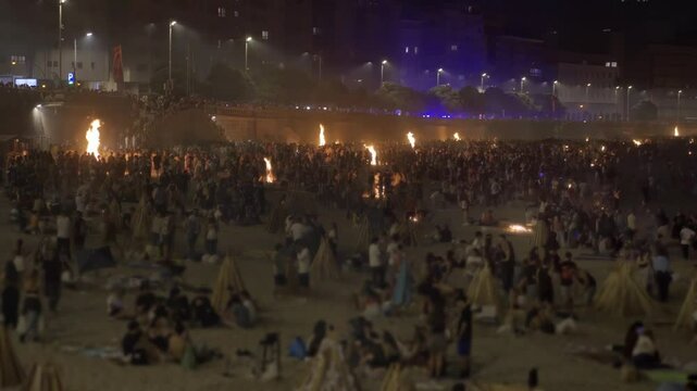 bonfires at st. John night fest in Coruna , Spain , with people unfocused on foreground  and controlled fire on beach at night , 4k video footage with focus in background