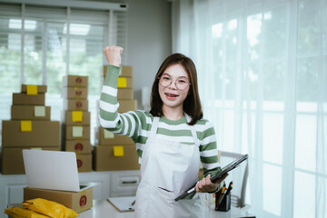 A young woman entrepreneur manages her online business from home, surrounded by parcel boxes, using a laptop, calculator, and notepad to handle shipping and inventory.
