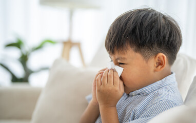 Young asian boy sneezing or blowing his nose and mouth with tissue, cold allergies or illness,...