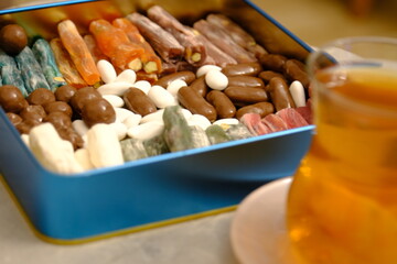 Eid candies. Traditional Turkish delights, almond candy and cocoa dragees in a blue metal gift box. Eid al-Fitr, Eid al-Adha. Close-up of a woman's hand taking almond candy from a box.