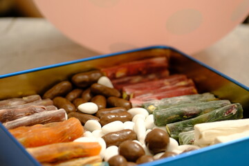 Eid candies. Traditional Turkish delights, almond candy and cocoa dragees in a blue metal gift box. Eid al-Fitr, Eid al-Adha. Close-up of a woman's hand taking almond candy from a box.