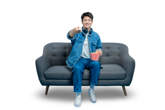 PNG,A young Asian man sits on a sofa with popcorn and points a TV remote at the camera, ready to start a movie.
