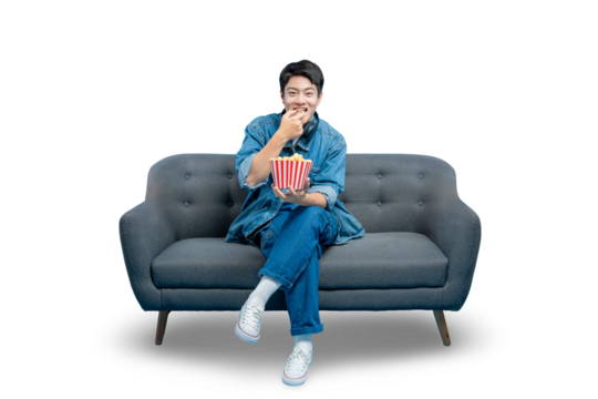 PNG,young Asian man eats popcorn while sitting cross-legged on a sofa, enjoying a movie night at home.
